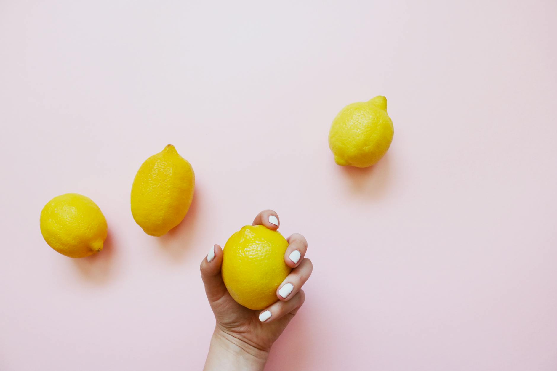 A hand holding a fresh lemon on a soft pink background, symbolizing renewed sensitivity and reset