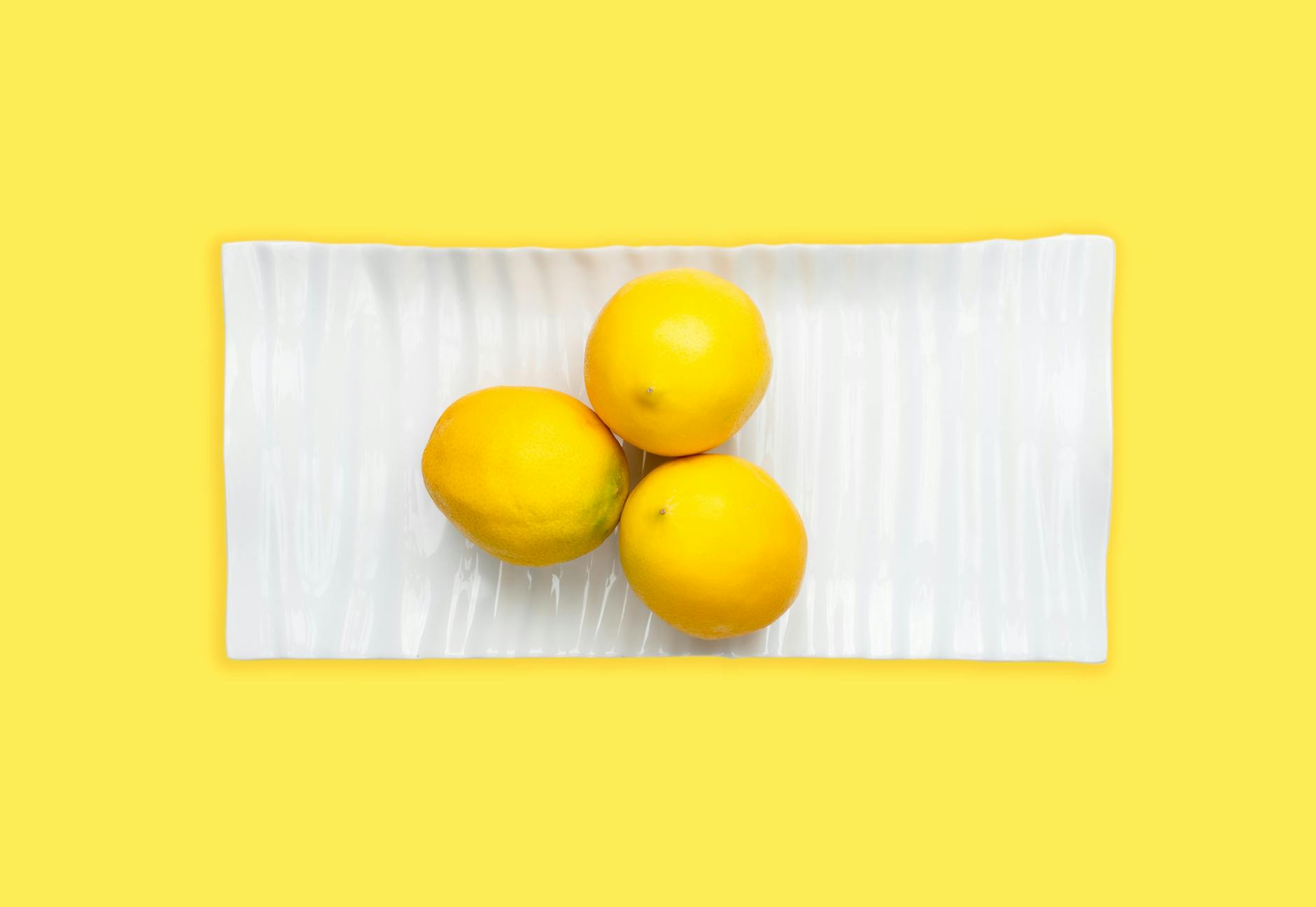 Fresh lemons on white plate with vibrant yellow background symbolizing renewal and sensation