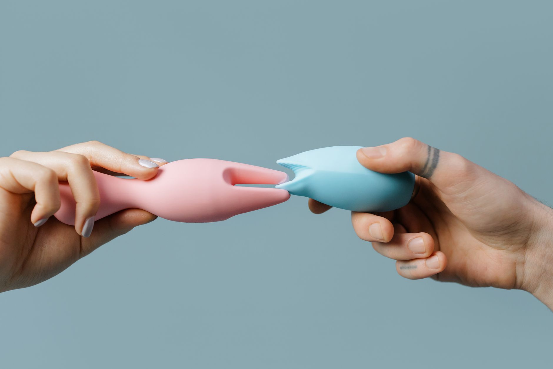 Hands holding pastel-colored silicone sex toys, representing personal pleasure and self-care