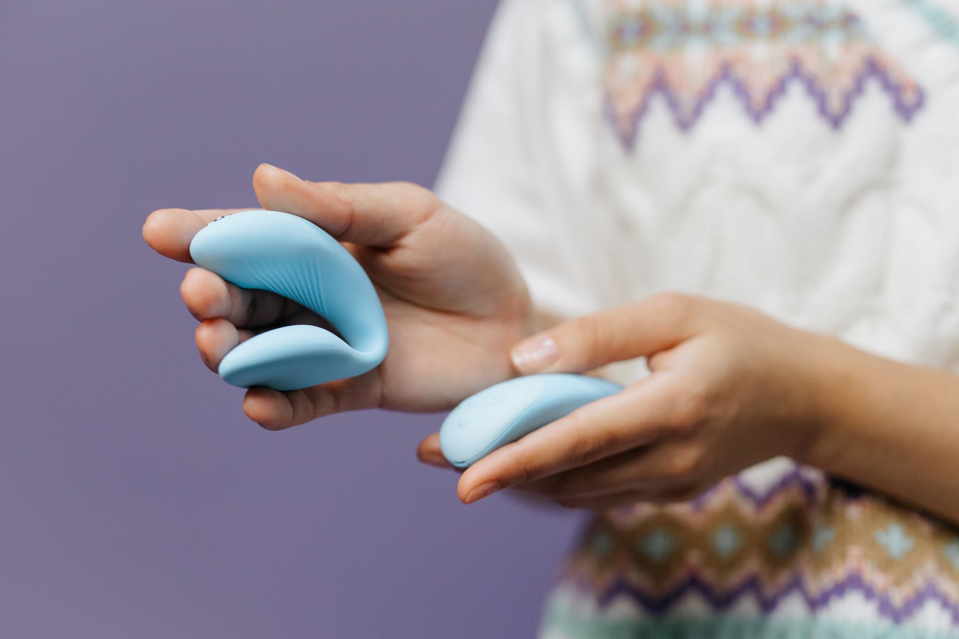 Hands holding a sleek blue vibrator against a purple background, symbolizing self-pleasure and intimacy.