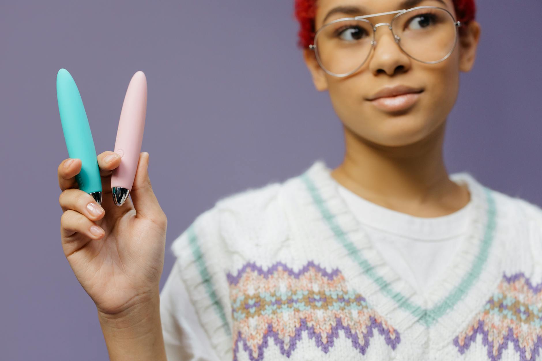 A young woman holding colorful vibrators against a purple background